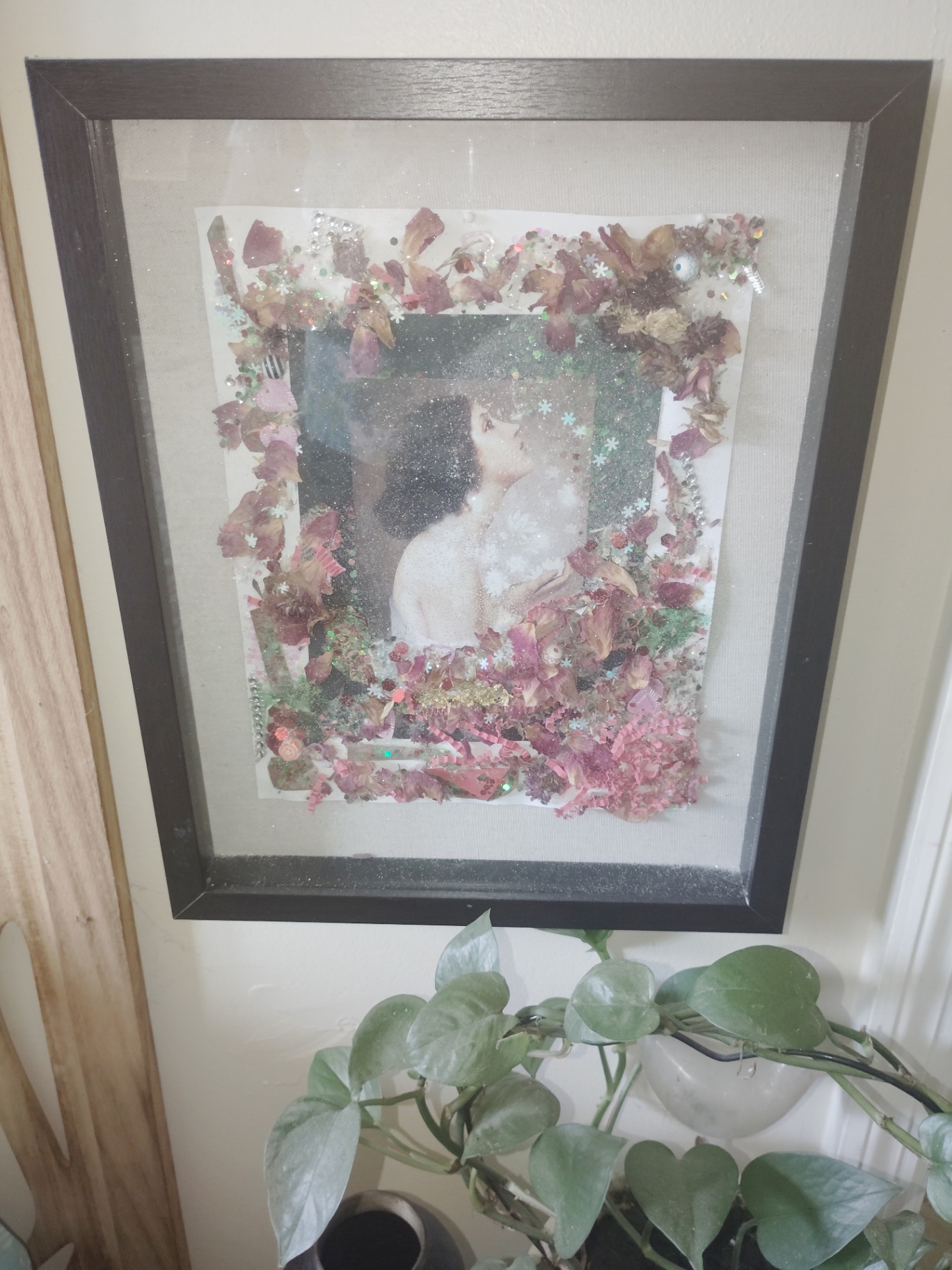 Framed Cat Nap Inn portrait artwork surrounded by dried florals, glitter, and pink embellishments beside a pothos plant
