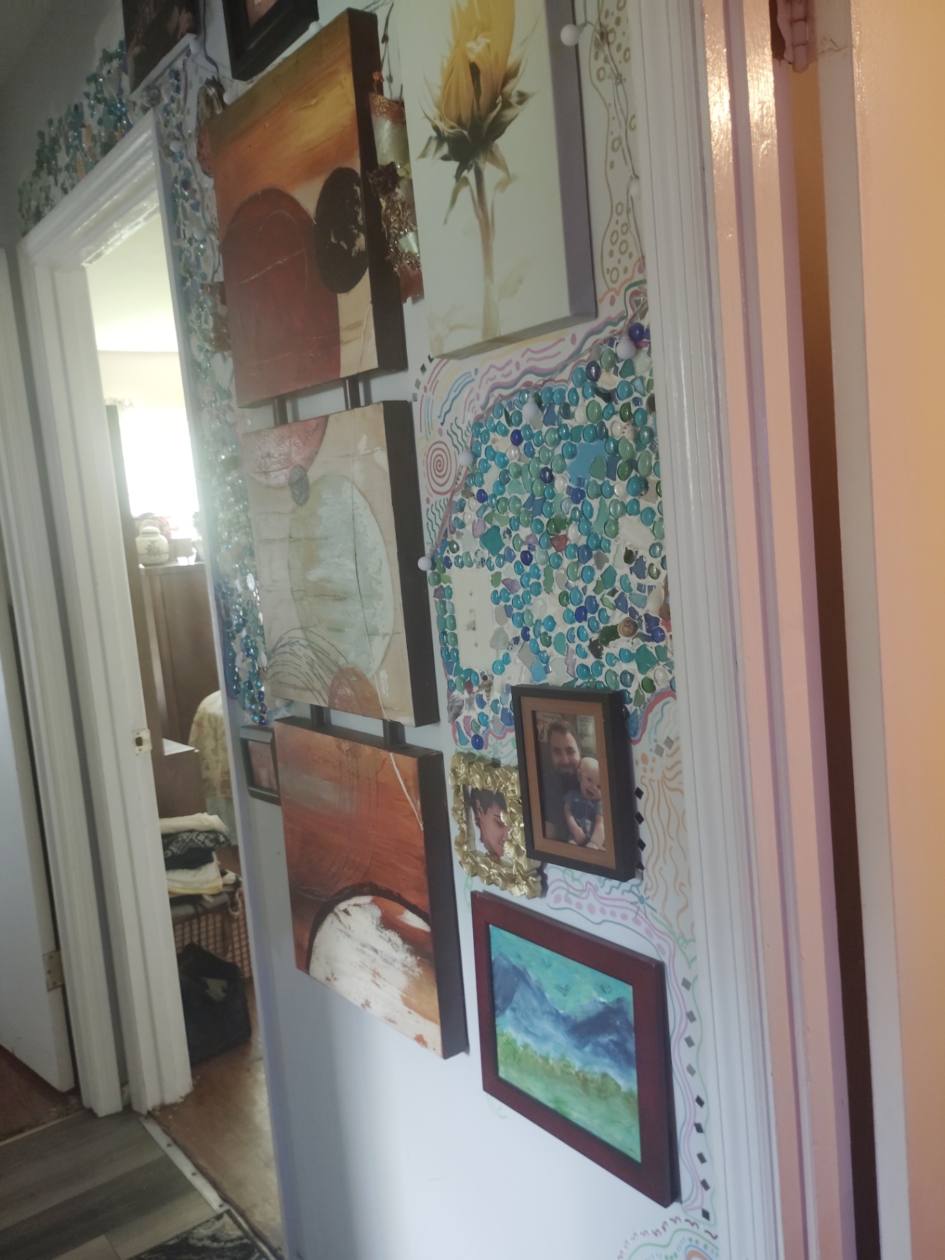 Hallway wall inside the Cat Nap Inn with handmade artwork, mosaic-like glass pieces, framed photos, and soft painted swirls